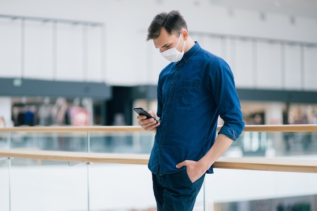 Young man in a protective mask reading a text message on his smartphone