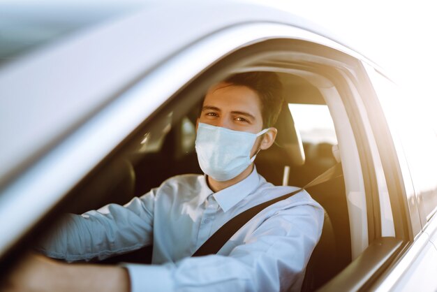 Giovane uomo in una maschera protettiva seduto in macchina