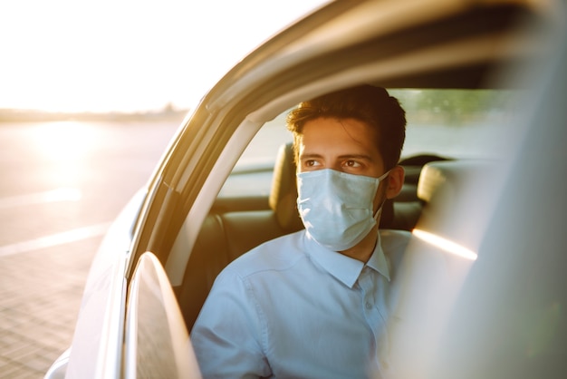 Giovane uomo in una maschera protettiva seduto in macchina