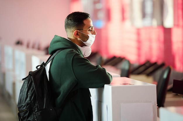 Foto giovane con maschera protettiva in piedi al banco di registrazione all'aeroporto