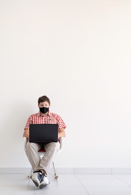 Young man in protective mask studying online keeping social distance using laptop