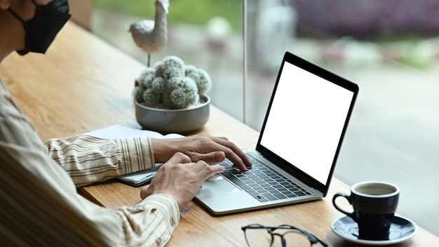 Young man in protective mask using laptop computer in coffee shop.