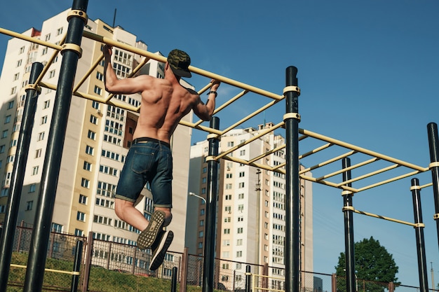 A young man pulls himself up sports ground, an athlete, training outdoors in  city