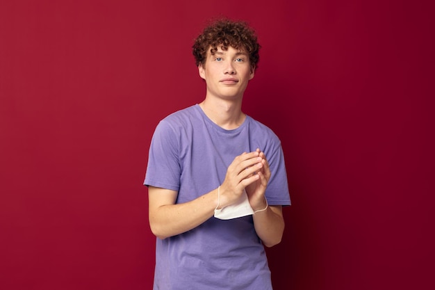 A young man in purple tshirts medical mask in hands safety red background unaltered