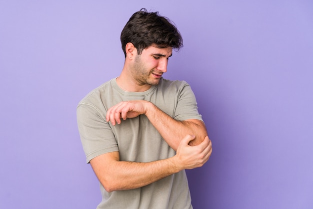 Young man on purple wall massaging elbow