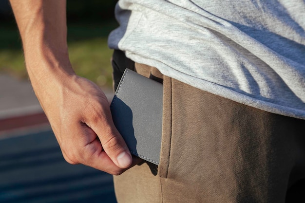 The young man puts a gray leather wallet in his back pocket