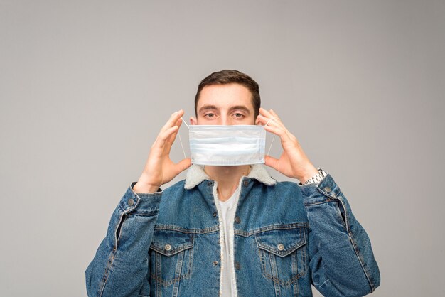 The young man puts on or takes off the medical mask. Stands on a light surface.