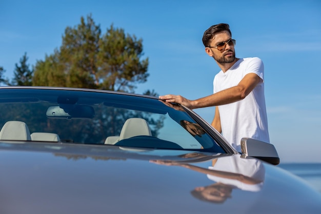 Young man putting hand on the car and looking away at daytime