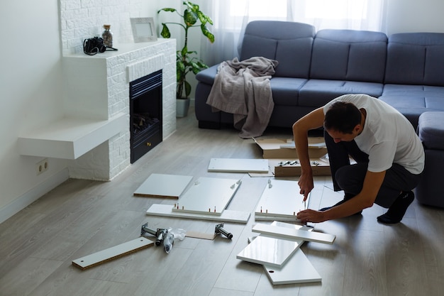 Photo young man putting self assembly furniture as they move into your new house.