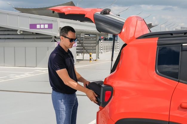 Young man putting suitcase in car trunk at parking