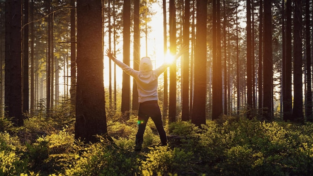 手を上げた若い男は森に立って、自然と日光を楽しんでいます