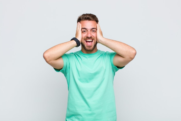 Young man raising hands to head, open-mouthed, feeling extremely lucky, surprised, excited and happy