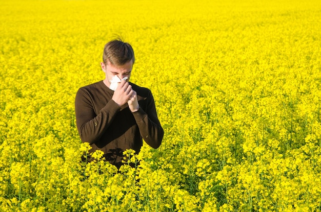 A young man in a rapeseed yellow field with a handkerchief suffers from an allergy