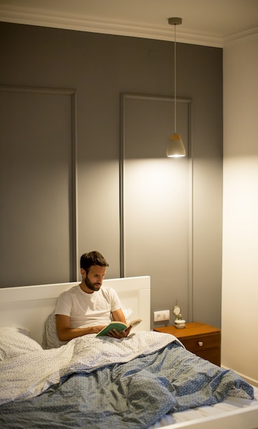 Young man reading book in bed