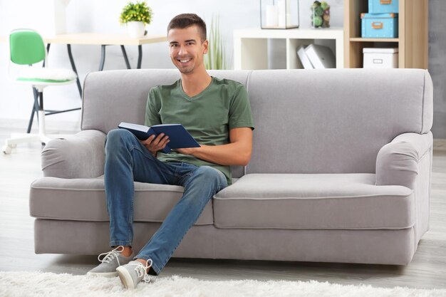 Photo young man reading book on sofa at home