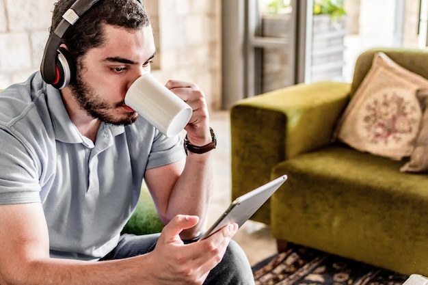 リビング ルームでの朝食時にタブレットでニュースを読んでいる若い男