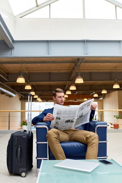 Young Man Reading Newspaper in Hotel Lobby