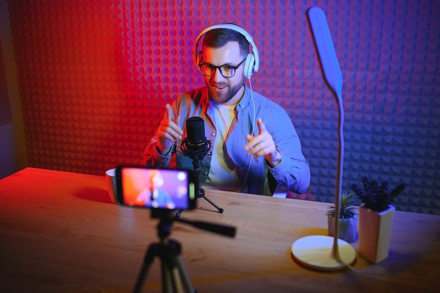 Молодой человек записывает или транслирует подкаст с помощью микрофона в своей небольшой студии вещания.