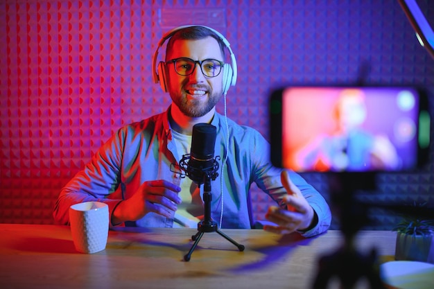 Young man recording or streaming podcast using microphone at his small broadcast studio Content creator