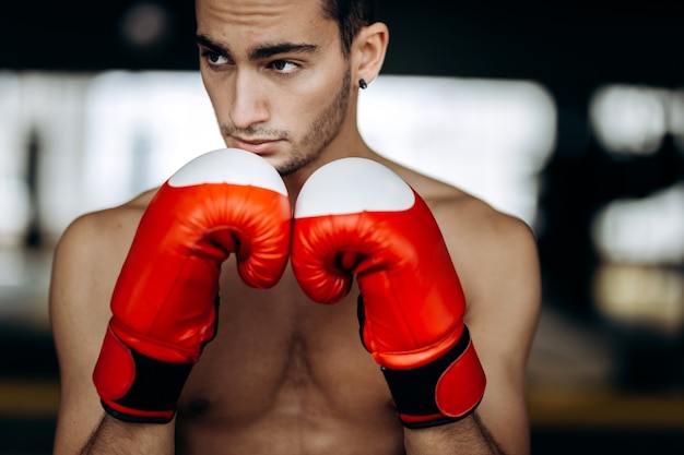 Young man in red boxing gloves on his hand is in the boxing gym