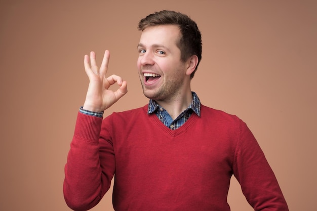 Young man in red sweater gesturing ok sign