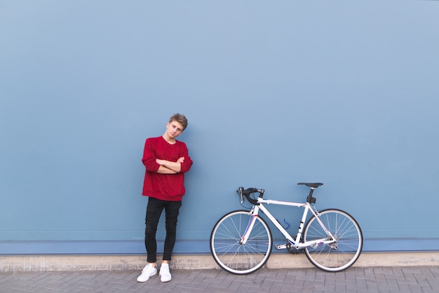 Young man in a red sweatshirt standing by a bicycle on a blue background