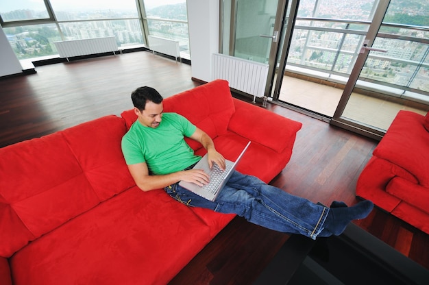 Young man relax on red sofa and work on laptop at home indoor