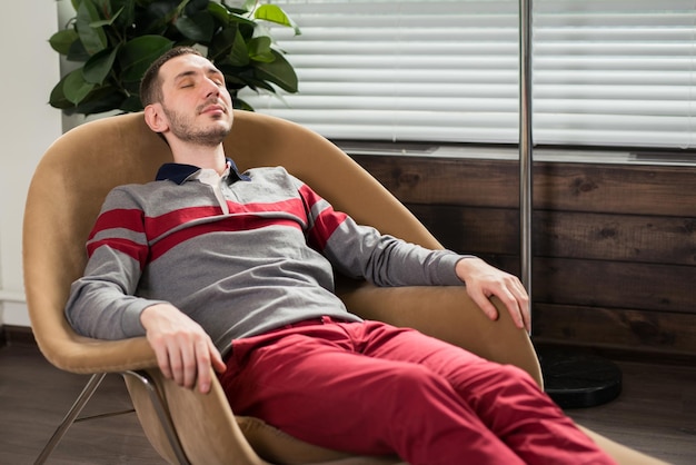 The young man relaxes lies in a chair with his eyes closed