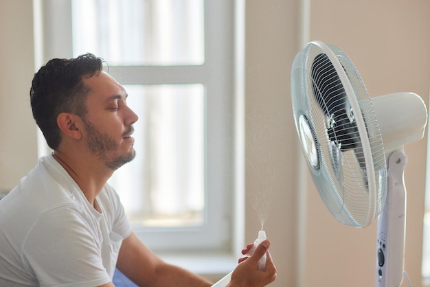 Young man relaxing under the air fan at home