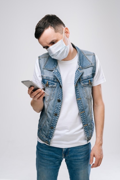 Young man in respiratory mask chatting with somebody while on white background. Prevention of virus infection. Concept of Coronavirus COVID-19 Pandemic.