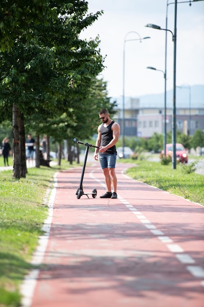 路上で夏に電動スクーターに乗って休んでいる若い男