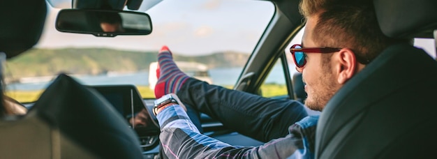 Young man resting feet up sitting on the car