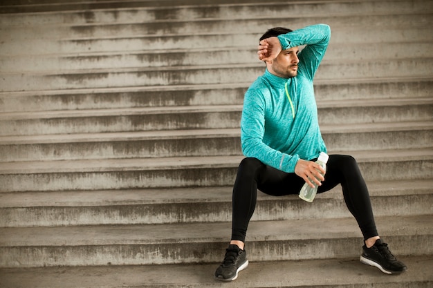 Young man resting during training with bottle of water in urban environment