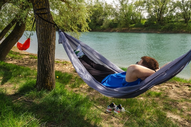 A young man rests in a hammock on the river bank