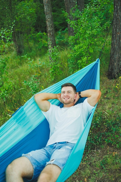 A young man rests in nature sitting in a tourist hammock Hammock for outdoor recreation Weekend rest of a lonely man in a deserted forest