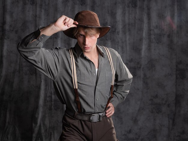 A young man in retro style an adventure character a guy in a hat and a gray shirt breeches with susp