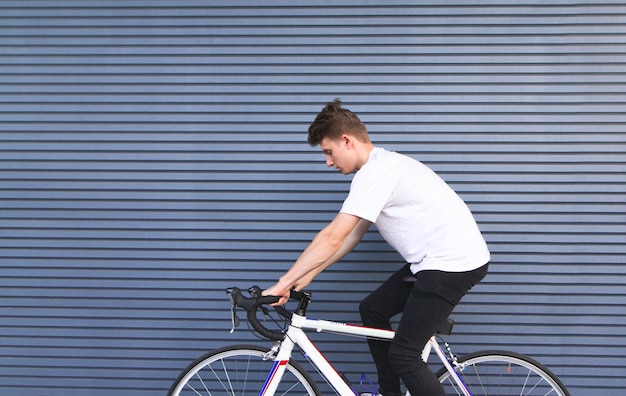 Young man rides a white highway bike against the background of the wall