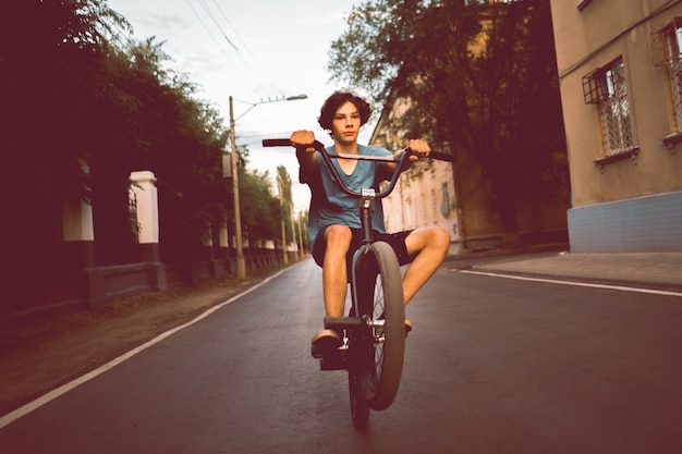 Giovane uomo in sella a una bici bmx su una ruota posteriore posteriore, facendo acrobazie in città