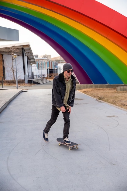 Photo young man riding a skateboard against composition with rainbow concept of lgbt style