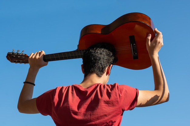 Young man rising an accoustic guitar in the sky