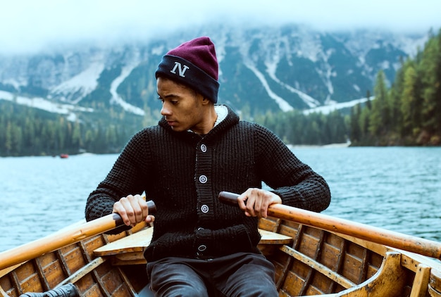 Photo young man rowing boat on lake against mountains