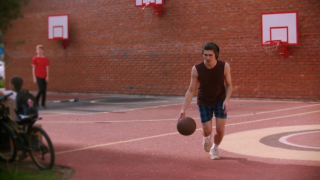 Молодой человек бежит по баскетбольной площадке и бьет по мячу