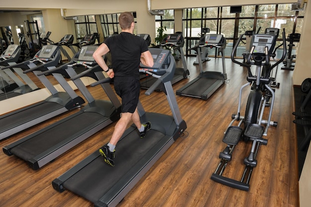 Young man running at treadmill in gym