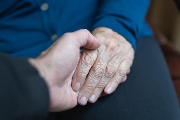 Photo young man's hand holding older woman's hand in caring and helping attitude.