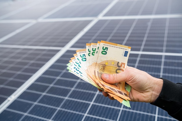 Young man's hand holds a euro for the installation of new solar panels