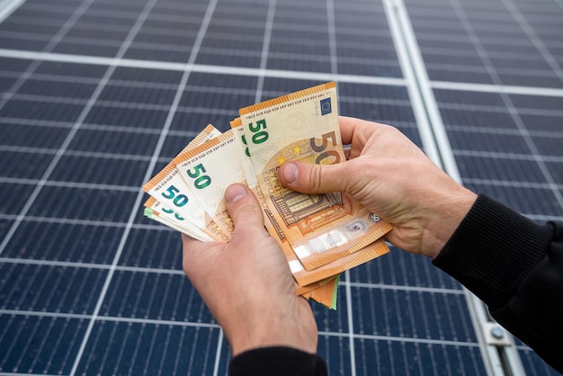 Young man's hand holds a euro for the installation of new solar panels