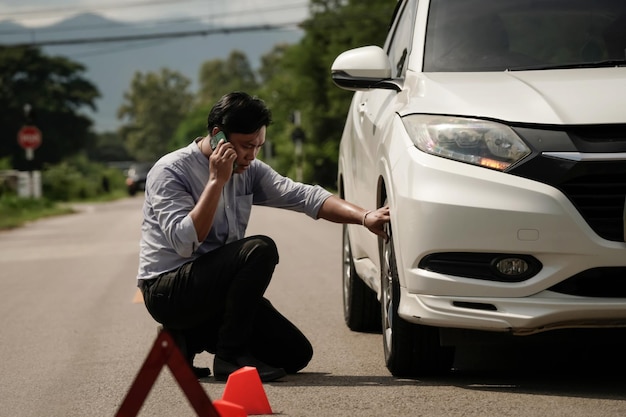 Photo young man's point of view sit on the road near a broken car and talk to the mechanic on the phone