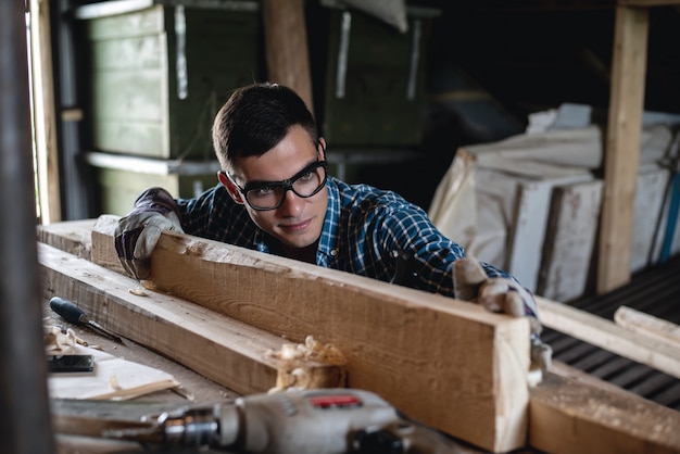 Young man in safety glasses and gloves checks the quality of the planed wooden board