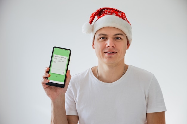 Young man in santa hat holds smartphone with electronic covid vaccination certificate