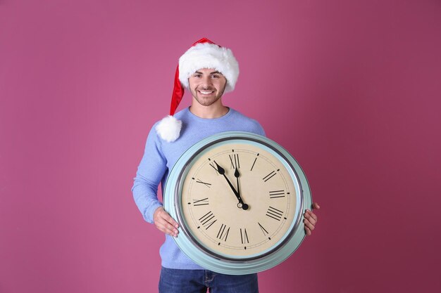 Young man in Santa hat with clock on color background. Christmas countdown concept